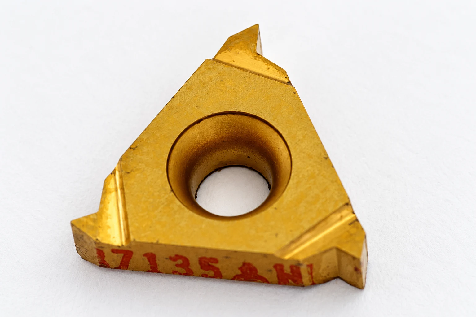 Triangular threading insert with a visible cutting tip; photo-based editorial edit