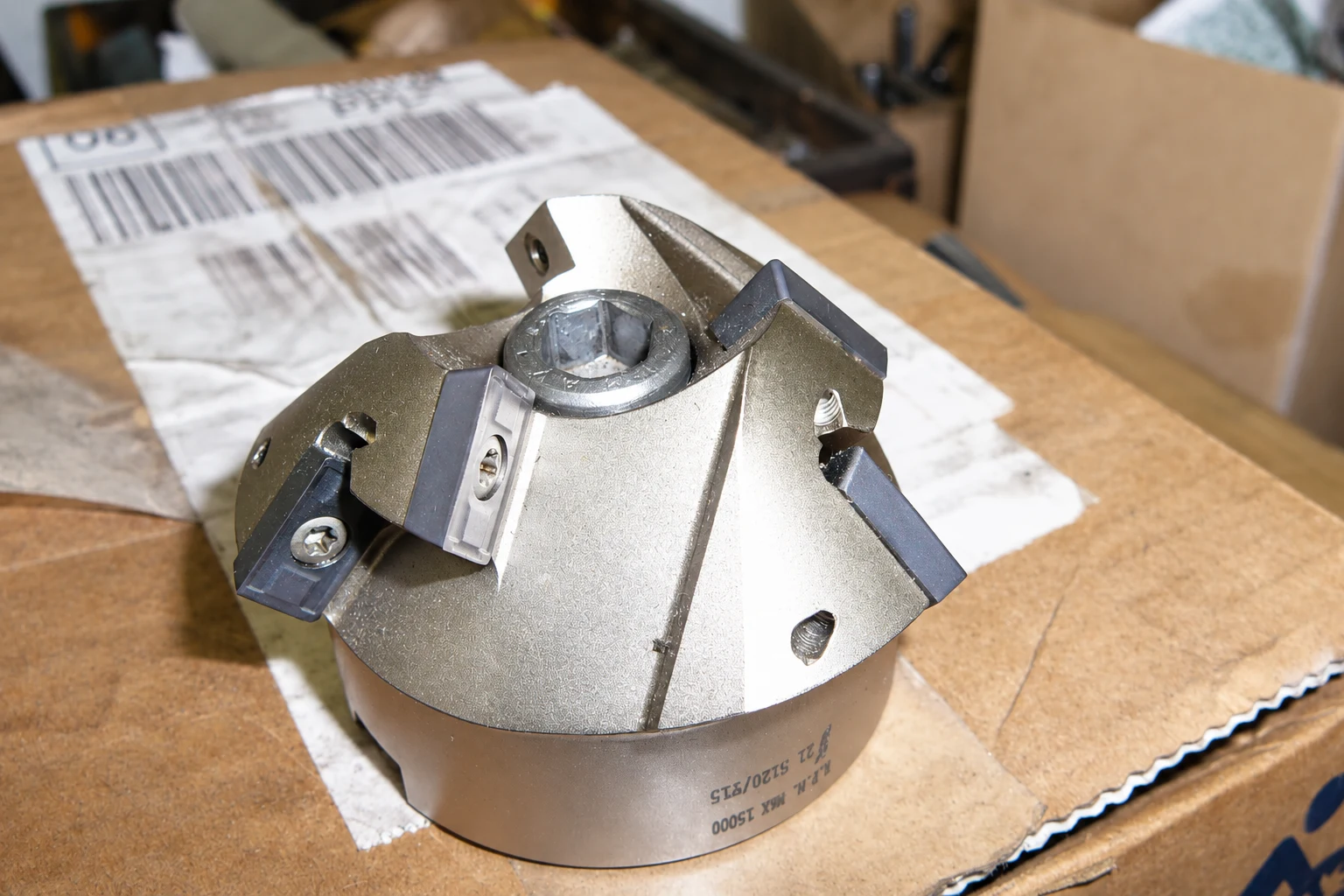 Face mill with seated inserts on a cardboard workshop surface; photo-based editorial edit