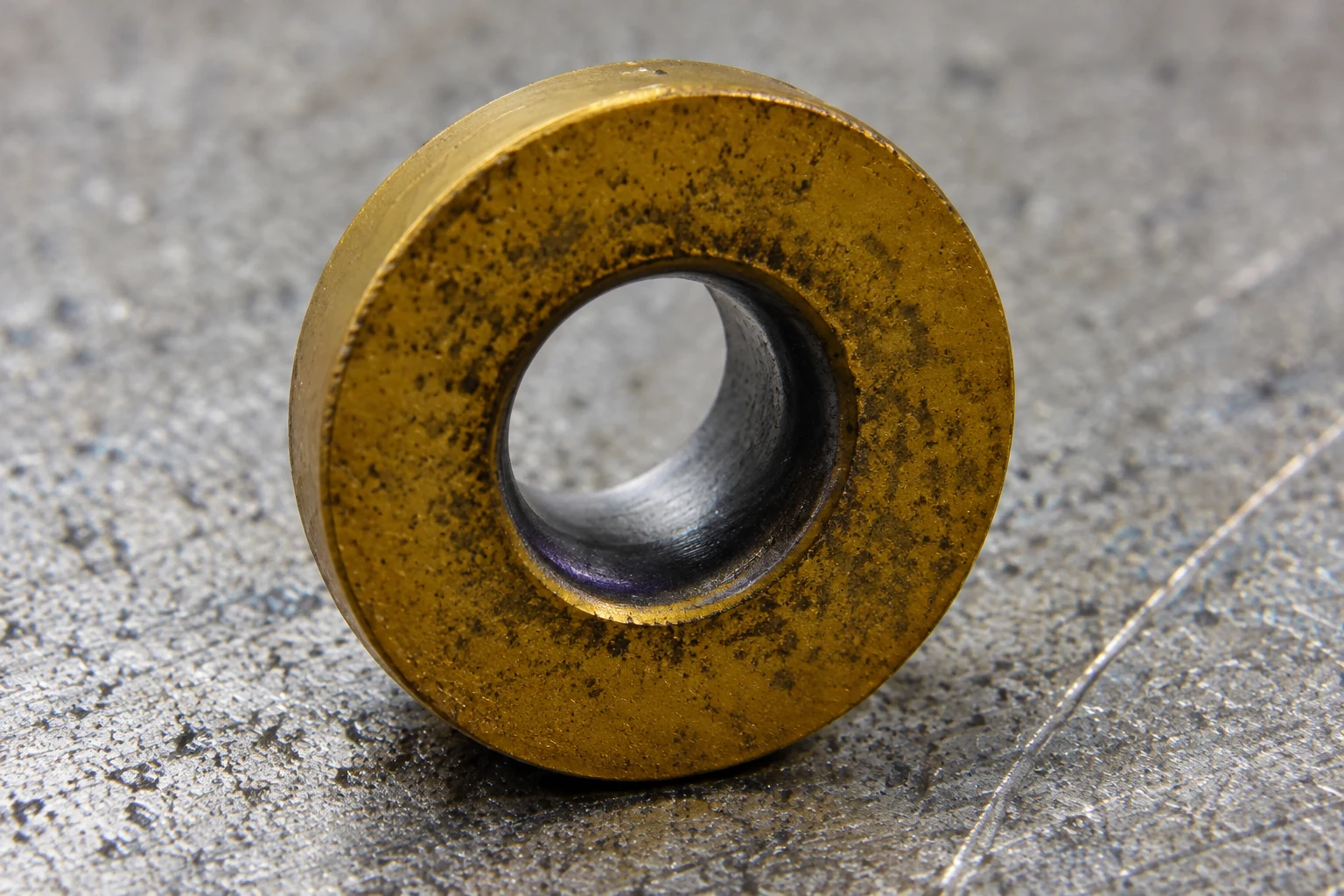 Close-up of a round coated cutting insert on a worn metal workbench; photo-based editorial edit