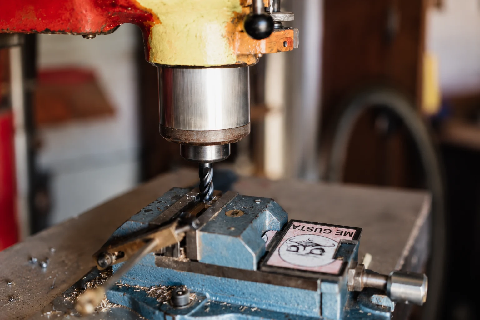 Close view of a drill and workpiece in a machine vise; photo-based editorial edit