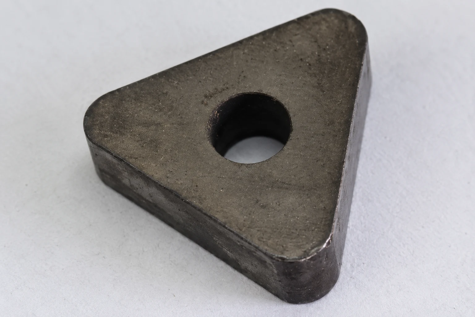 Dark triangular cutting insert with center hole on light paper; photo-based editorial edit