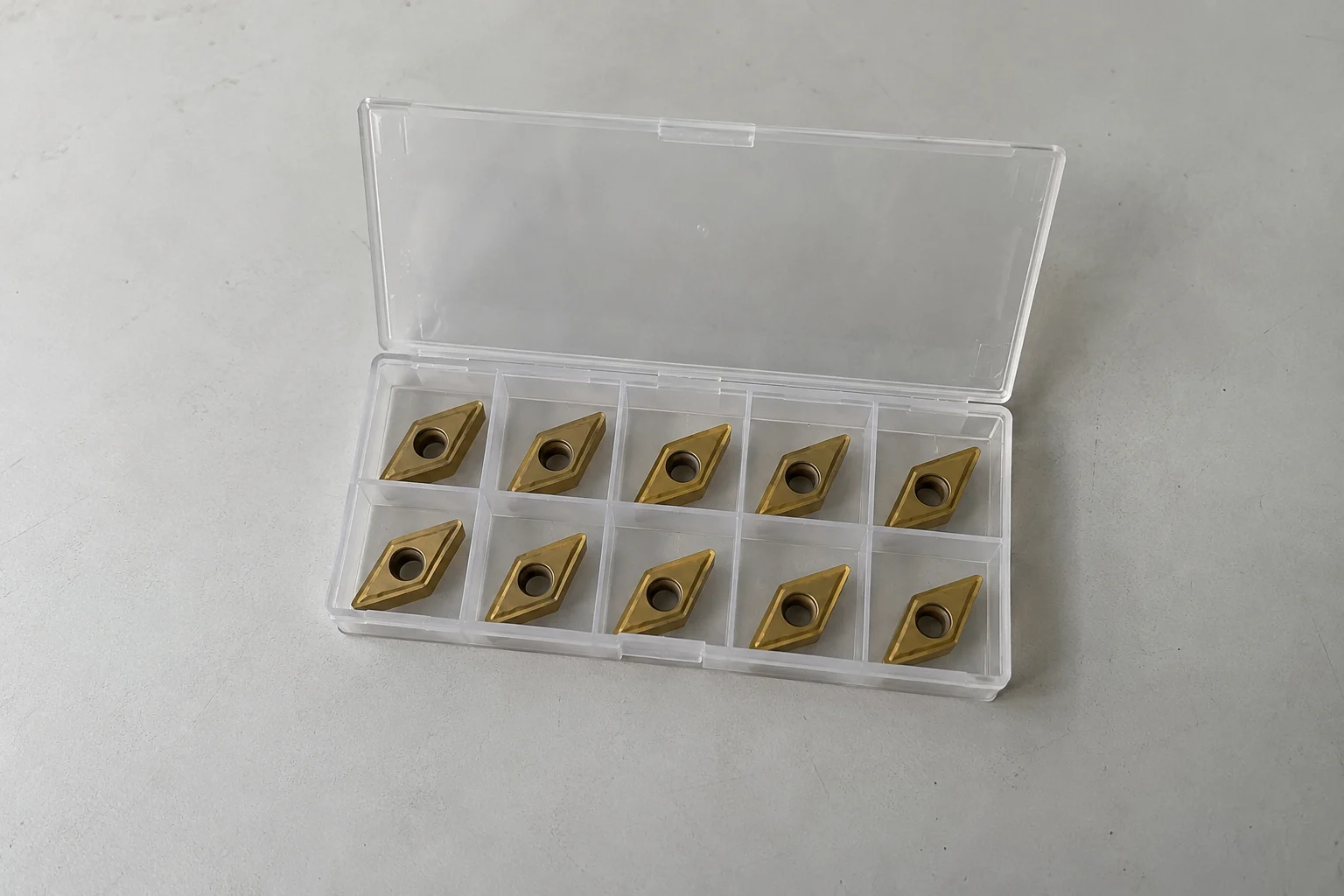 An open plastic box containing ten carbide turning inserts
